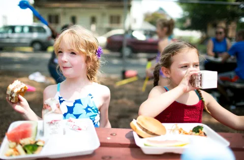 Two little girls eating lunch at a table outdoors